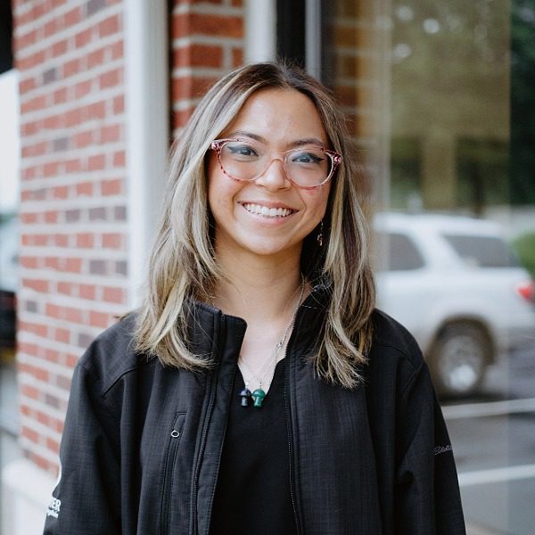 female with shoulder length brown hair with highlights, wearing glasses and a black jacket