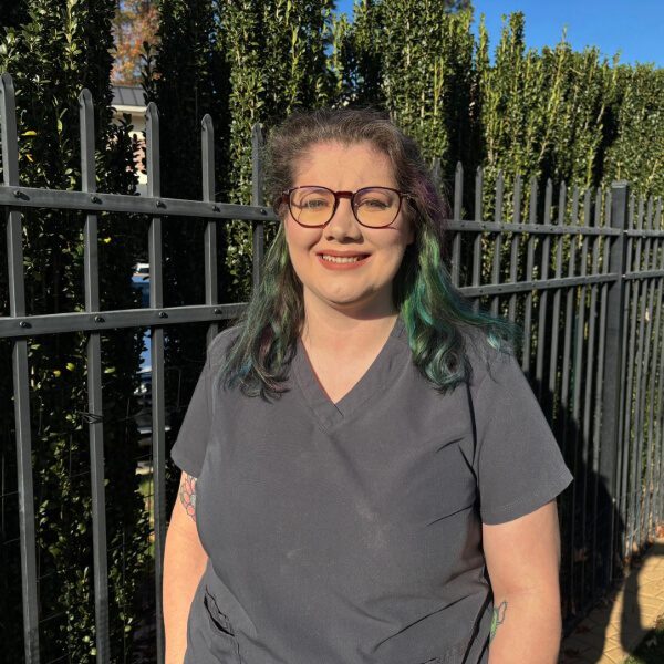 Katie McQuaig, female vet tech with brown and green hair, wearing glasses and gray scrubs