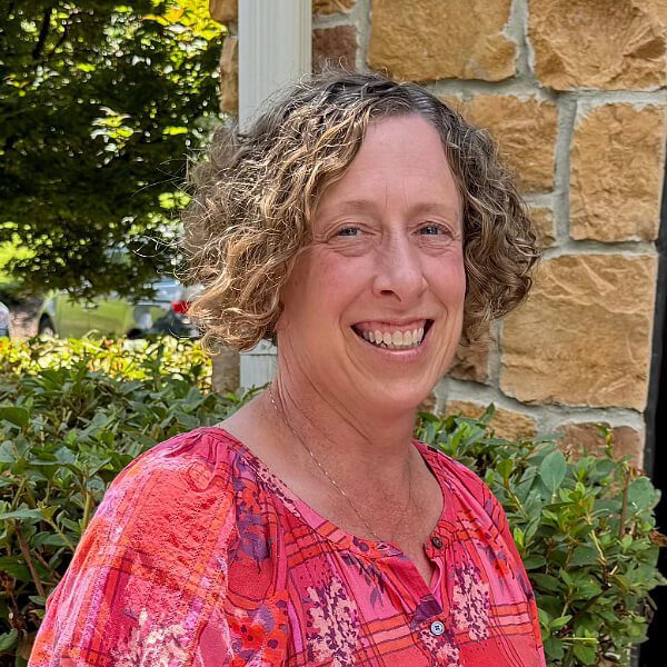 Susan female with short curly hair waring a pink button collared shirt